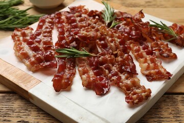 Slices of tasty fried bacon and rosemary on wooden table, closeup