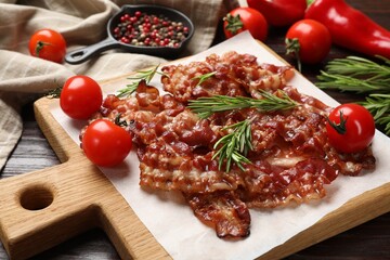 Slices of tasty fried bacon, rosemary, tomatoes and peppercorns on wooden table