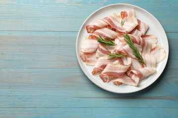 Slices of raw bacon and rosemary on light blue wooden table, top view. Space for text
