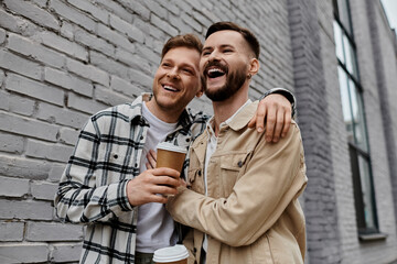 A gay couple in casual attire standing side by side near a brick wall.