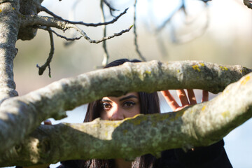 Black eyes of a young girl between the trunks of a leafless tree.