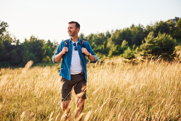 Mid adult man walking alone with backpack in countryside during summer weekend trip