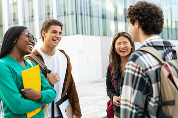 Group of four students meeting in front of the university building after lecture, talking having fun