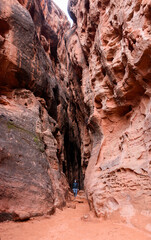 A male hiker walking in Jenny's Slot Canyon surrounded by steep red Navajo sandstone rock walls - Snow Canyon State Park, St George, Utah, USA