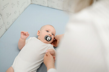 Small newborn baby lies in bed, mom gives pacifier to baby. Concept of infancy, childhood, child...