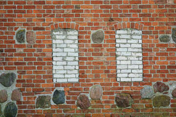 A fragment of the wall of an old red brick medieval church. There are two windows, bricked up with white sand-lime brick. Background.