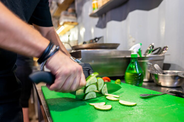 A person skillfully slices cucumber on a green cutting board, surrounded by kitchen utensils and...