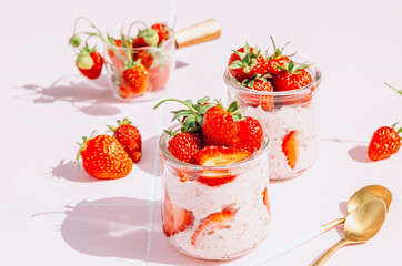 A delightful and healthy breakfast of overnight oats with yogurt and fresh strawberries, beautifully presented in glass jars on a vibrant pink tile table. Bathed in natural sunlight