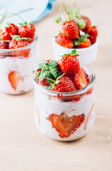 A wholesome and nourishing breakfast of overnight oats with yogurt and fresh strawberries, served in glass jars on a rustic wooden table. Soft, diffused light creates a warm and inviting atmosphere