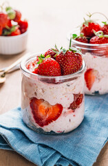 A wholesome and nourishing breakfast of overnight oats with yogurt and fresh strawberries, served in glass jars on a rustic wooden table. Soft, diffused light creates a warm and inviting atmosphere
