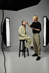 A woman sits on a stool, receiving makeup from a talented man.
