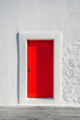 A vibrant red door stands alone in the center of a white wall, casting a slight shadow. The design is simple and clean, highlighting the door as the focal point.