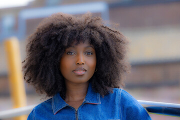 A stunning portrait of a beautiful woman with natural afro hair in a denim jacket, captured outdoors