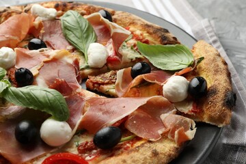 Tasty pizza with cured ham, olives, mozzarella cheese, sun-dried tomato and basil on table, closeup