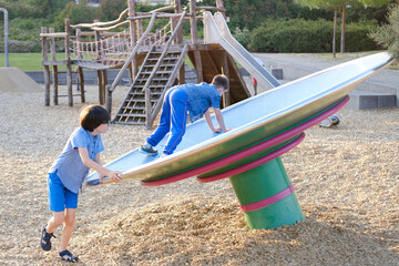 children, two boys 9-10 years play in playground, try to keep balance on balance wheel, fun piece...