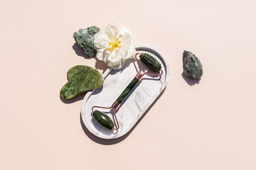 Green Jade Roller Massager, Gua Sha Scraper lie on an oval marble decorative tray among natural...