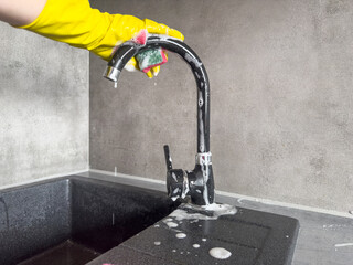 Woman's hands in yellow protective rubber gloves wiping a kitchen faucet