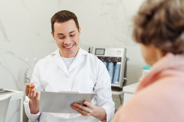 Obraz premium Attractive man, doctor, cosmetologist communicating with senior woman, patient, talking