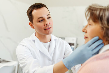 Fototapeta premium Professional cosmetologist man examines patient's face, touching, consulting, wearing medical gloves