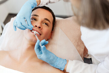 Closeup, beautician doctor holding injection, lip plumping to attractive young man, patient