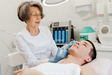 Smiling senior mature woman doing cosmetic procedures in modern clinic, removing wrinkles near eyes