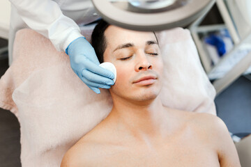 Man getting cosmetic procedures in cosmetic clinic. Cosmetologist caring of patient's facial skin