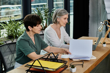 Two women engrossed in work on a laptop at a table.