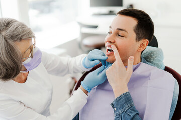 Attractive young man, patient having toothache, showing teeth to professional, senior doctor