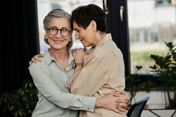 Two women hugging tenderly in front of a window.