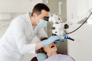Professional dentist doctor, man treating teeth using dental microscope, checking senior woman
