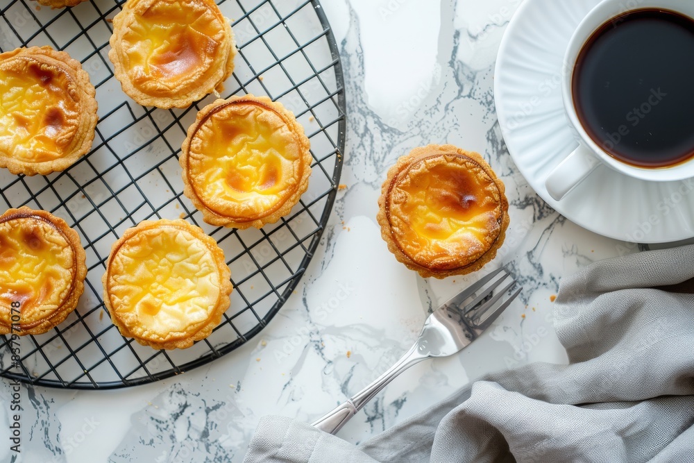 Wall mural Traditional Portuguese egg tart dessert Pasteis Pastel de nata on a cooling rack and ceramic plate with a fork, a cup of black coffee over a white marble background