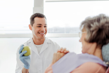 Smiling, attractive man, professional doctor, dentist holding apple talking with senior woman