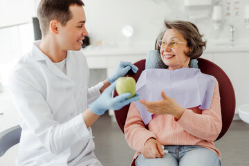 Happy man, professional doctor, dentist holding apple talking with patient. senior, mature woman