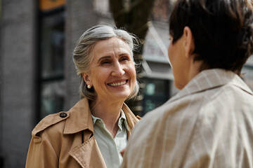 Two women smiling in stylish trench coats.