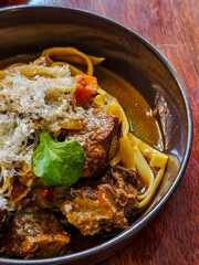 Real spaghetti fettuccine pasta dish in traditional italian food style with beef stew and gravy sauce serve in dark bowl in close up picture and wood table background