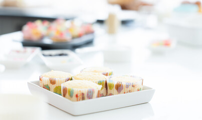 Fresh cakes baked from oven. Homemade cupcakes in paper cups in kitchen at home. Cupcakes with decorations, flour, sugar and decorating icing candy on table. Selective focus