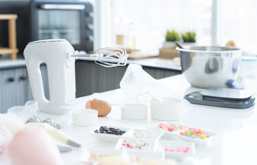 Selective focus on electric mixer. Mixing bowl, measuring spoons, scales, sugar, flour, eggs,...
