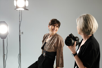Middle aged lesbian couple in a photo studio. One woman, the photographer, is taking a picture of...