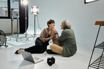 A middle-aged lesbian couple, one as a photographer and the other as a model, sitting in a photo studio.