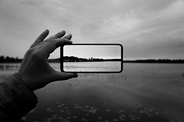 Cropped hand holding a mobile phone while photographing a lake