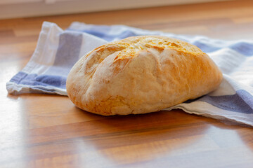 whole loaf of fresh white bread on kitchen towel on a wooden table close-up