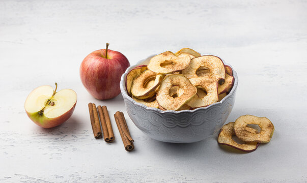Homemade dried apples with cinnamon, apple chips in a bowl with cinnamon sticks on a light gray background. Delicious healthy snack