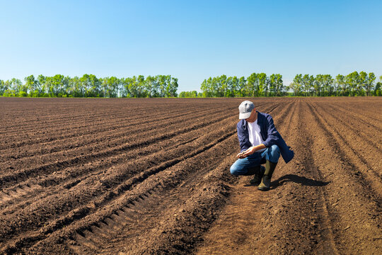 man agronomist crouching inspecting the quality of soil in the field.