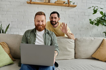 Two men, one bearded, sitting on a couch, focused on a laptop screen in a cozy living room setting.