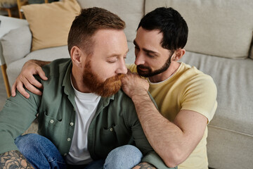 A cozy scene of a gay couple with beards, sitting closely together on the backrest of a couch in...