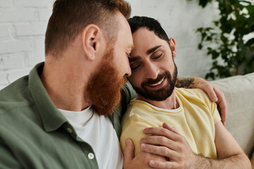 Bearded gay couple relax together on sofa, enjoying quality time in stylishly decorated living room.