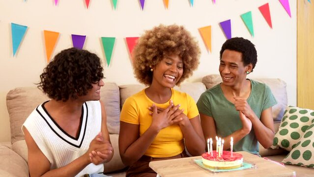 Three multiracial males and female friends singing and clasping hands celebrating birthday at home