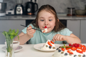 Little girl with a big spoonful of delicious berry dessert or cake sitting at the table against the...
