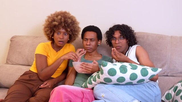 Multi-ethnic friends enjoying movie night eating pop corn on the sofa together