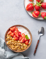 Natural yogurt with granola and strawberries in a wooden bowl on a blue background with fresh berries and napkin.
